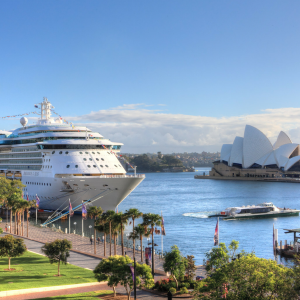 A large cruise ship docked at a harbor near the Sydney Opera House on a sunny day with clear skies and calm water.