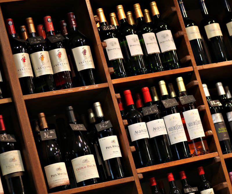 Shelves filled with assorted bottles of red wine arranged in rows, each with labeled tags indicating prices.