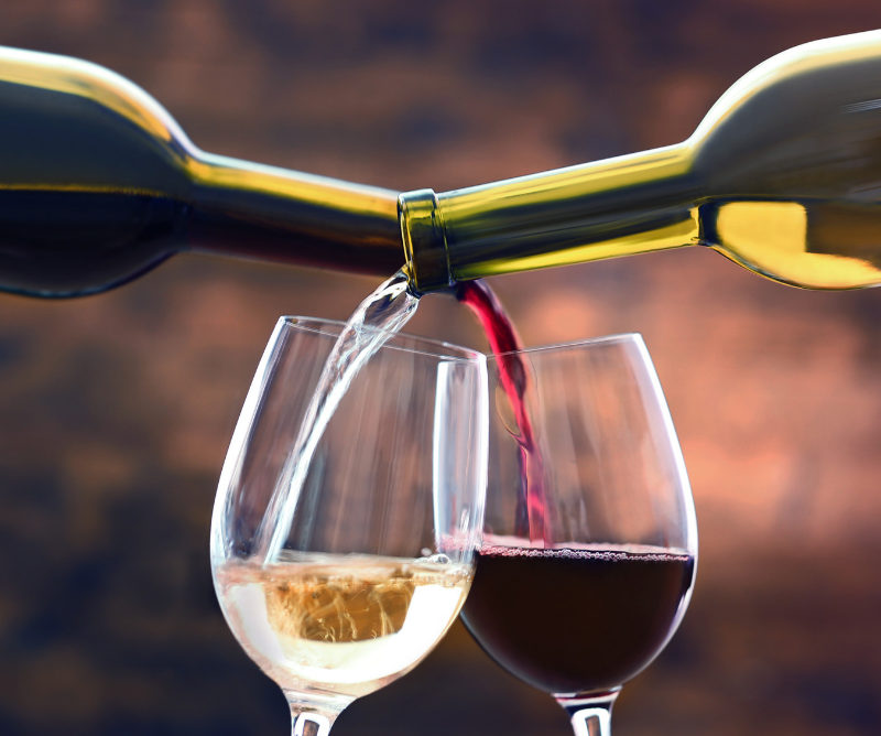 Two wine bottles, one with white wine and one with red wine, are pouring their contents into separate wine glasses against a blurred background.