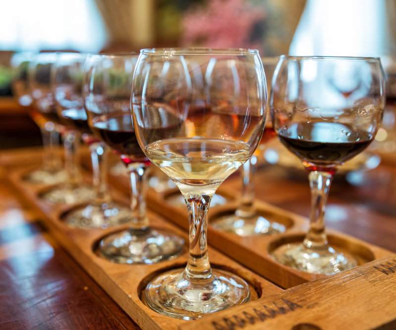 A close-up of several wine glasses filled with different types of wine, arranged on a wooden tasting tray on a table.