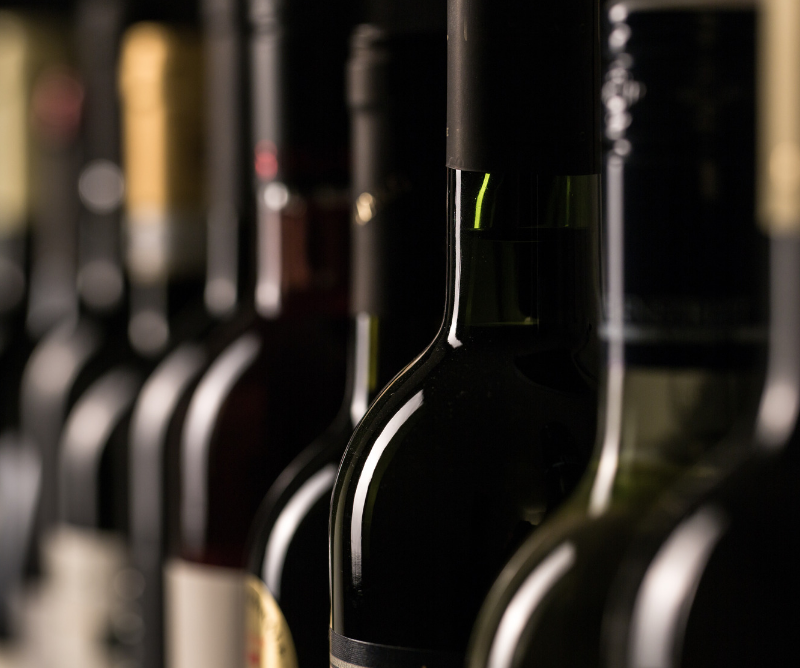 Close-up of several wine bottles standing in a row, photographed from the neck up, with varying colors and labels slightly out of focus.