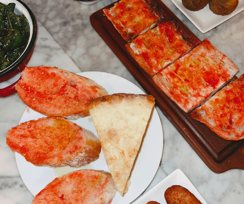 A plate with slices of bread topped with tomato, a slice of focaccia, rectangular pieces of tomato-topped flatbread, and small fried items on a marble table.