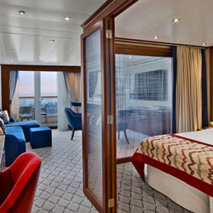 A modern hotel room with a bed, seating area, large window, and partially open glass doors separating the spaces.